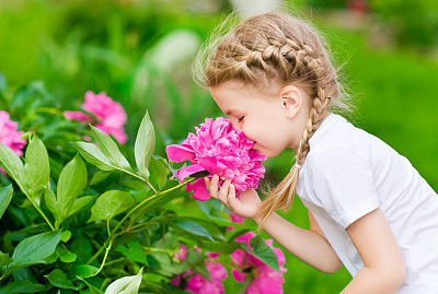 Blonde girl with braided hair smelling pink flower in garden