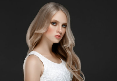 Amazing woman portrait. Beautiful girl with long wavy hair. Blonde model with hairstyle over black background