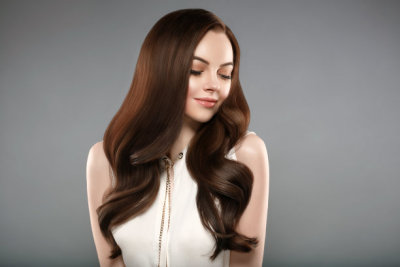 Beautiful shine hair woman with manicure nails hand. Brunette with long hair and healthy skin over gray background.