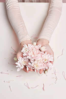 Fashion art portrait woman in summer dress and flowers in her hand with a bright contrasting makeup. Creative beauty photo girls sitting at table on a contrasting pink background with colored shadows