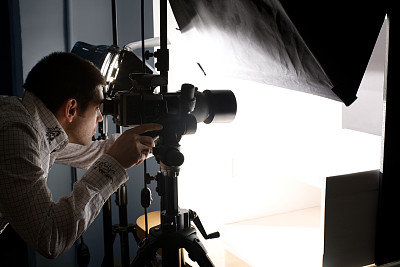 Photographer Looking Through Viewfinder Making Adjustments to Camera In Studio