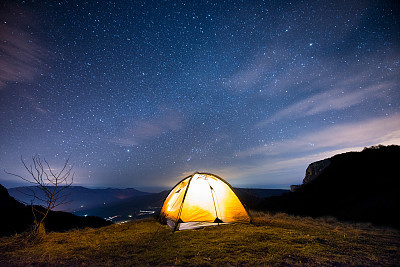 Glowing tent in the mountains under a starry sky