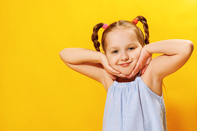 Closeup portrait of a cute attractive little child girl with pigtails out of hair over yellow background.