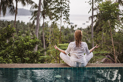 Rear view of a wet woman meditating at the edge of a swimming pool.