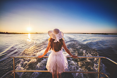 Rear angle view female on the back of a moving boat at sunset