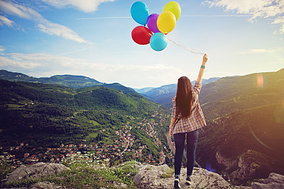 Girl with baloons is standing on the edge