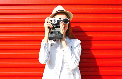 Fashion pretty young woman taking picture on retro camera over colorful red background