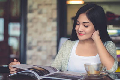 Beautiful attractive young Asian woman reading a magazine at cafe in the morning