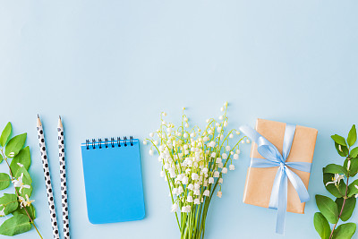 Flat lay blogger or freelancer workspace with a notebook, gift box and lily of the valley flowers on a blue background