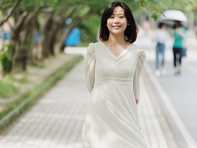 Portrait of elegant Chinese girl in white and green dress walking on sunny road in campus, smiling at camera friendly, Outdoor fashion portrait of glamour young Chinese cheerful stylish woman.