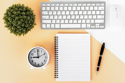 office desk with potted plant, computer keyboard and mouse, alarm clock, note pad and pen