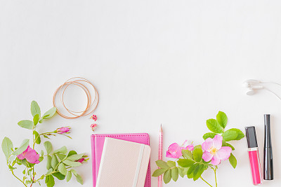 Flat lay blogger or freelancer workspace with a notebook, pink flowers and green leaves on a white background