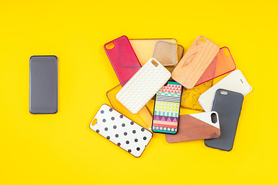 Pile of multicoloured plastic back covers for mobile phones on yellow background with a phone on the side