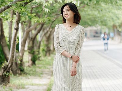 Portrait of elegant Chinese girl in white and green dress walking on sunny road in campus, smiling at camera friendly, Outdoor fashion portrait of glamour young Chinese cheerful stylish woman.