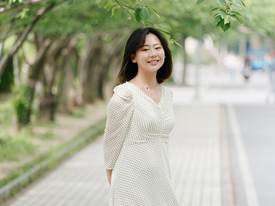 Portrait of elegant Chinese girl in white and green dress walking on sunny road in campus, smiling at camera friendly, Outdoor fashion portrait of glamour young Chinese cheerful stylish woman.