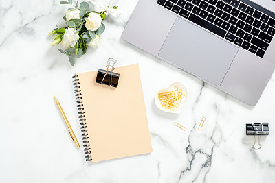 Flat lay home office desk. Women workspace with laptop computer, diary, flowers bouquet, golden accessories on white marble background. Top view feminine background. Beauty blogger workplace concept.