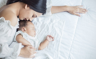 Close up portrait of beautiful young asian mother kissing her newborn baby sleep in bed.