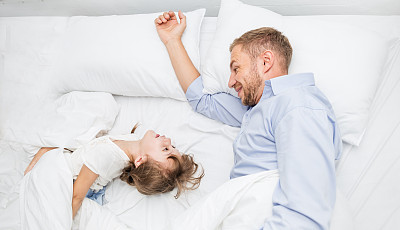Father and daughter laughing bonding in bed. Portrait of caucasian daddy and little girl spend time sleep in bedroom home.