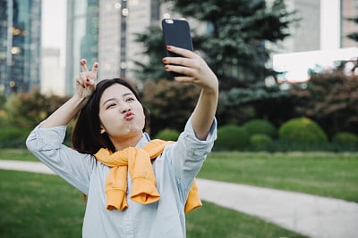 Beautiful Asian girl taking selfie with smart phone at park,Shanghai,China
