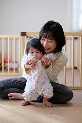 Baby practicing to stand up with mother at home