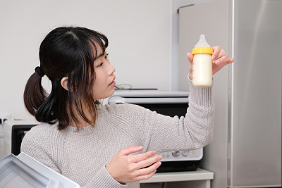 Mother looking at baby bottle in kitchen