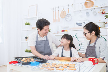 Portrait of little asian girl and her parents baking cake and cookies together in the kitchen. Happy asian family and motherâs day concept