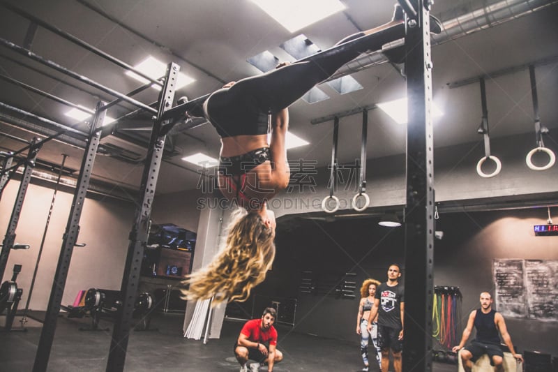 Ragazza bionda con fisico atletico durante allenamento di pull ups con spaccata, testa all'ingiù