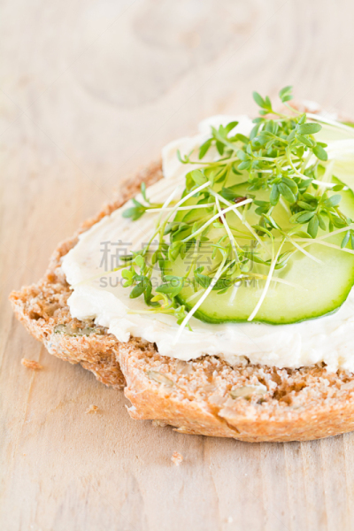 Eine Scheibe Brot belegt mit Frischkäse, Gurke und Kresse