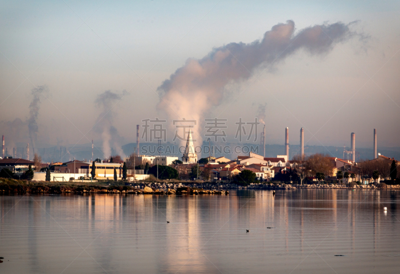 Un matin calme au bord de l'étang de Berre.
Les usines pétrochimiques fonctionnent et rejettent des fumées.
La ville se reflète dans l'étang.