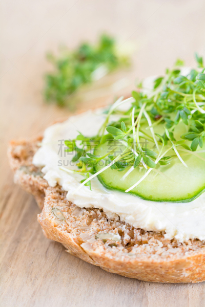 Eine Scheibe Brot belegt mit Frischkäse, Gurke und Kresse