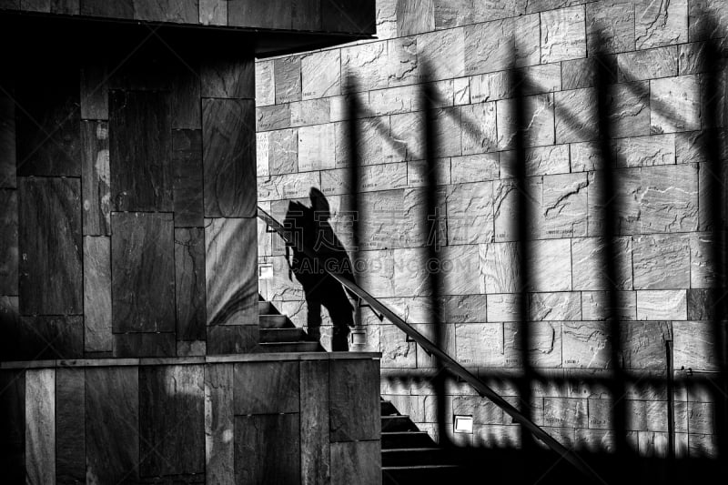 Photo prise au 'Grand Théâtre de Provence' à Aix en Provence.
Un escalier mène vers le théâtre.
Un personnage, dont on ne distingue que l'ombre, descend cet escalier.
Les ombres de la grille se détachent sur le mur.
Photo en noir et blanc