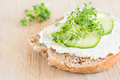 Eine Scheibe Brot belegt mit Frischkäse, Gurke und Kresse