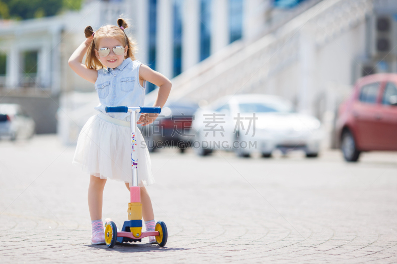 A nice little girl is riding alone on a children's scooter in a city in the summer