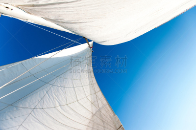 White yacht sails in sunlight on blue cloudy sky background.