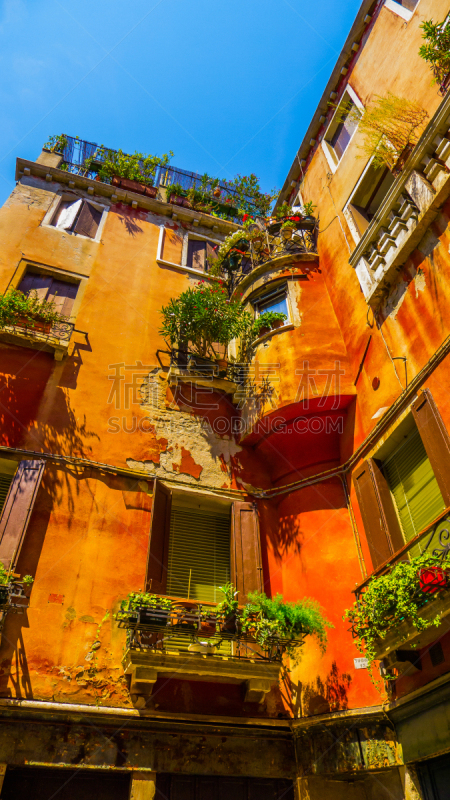 Balconies with beautiful plants and bright colors: old residential orange house of the historic district of Venice – summer photo with clear blue sky