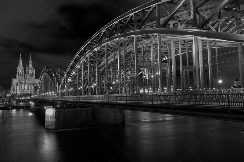 Kölner Dom, Hohenzollernbrücke Panorama mit dunklem Himmel in Schwarz Weiß, Blick über den Rhein auf das berühmte Kölner Motiv dessen Brücke zum Kölner Hauptbahnhof und zur Altstadt führt.