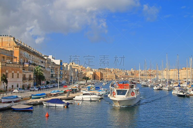 The photo was taken in the month of January in Malta. The picture shows a boat cruising the island’s harbor along moored yachts and boats.