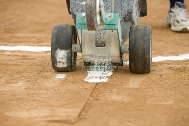 A field applicator is being used to dispense a dry chalk baseball batter’s box line which intersects the foul line to the right, in preparation for a game.