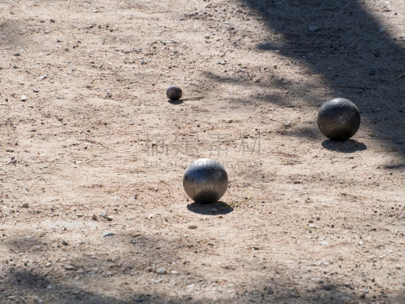 Petanque balls on the ground. Pétanque is a form of boules where the goal is to toss or roll hollow steel balls as close as possible to a small wooden ball called a cochonnet.