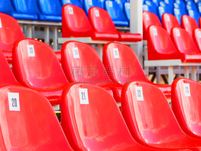 Tribune of stadium. Red and blue numbered empty plastic armchairs. Seats for spectators stand in a row. Passage between tribunes