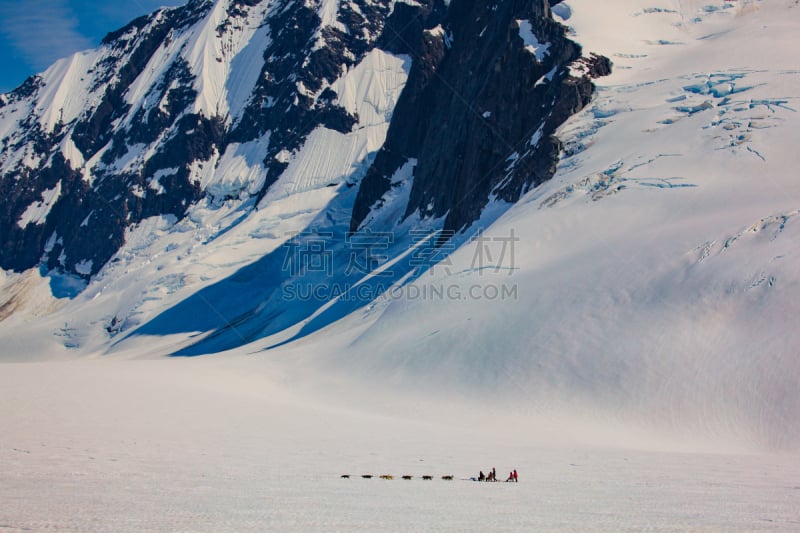 dogsled dwarfed by massive peaks