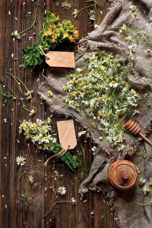 Close-up photo of camomile and St. John’s wort flowers on canvas. Top view on vintage wood background