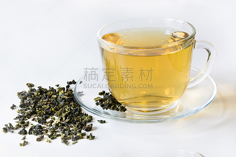 Glass cup with green tea and dry leaves of green tea on white background.