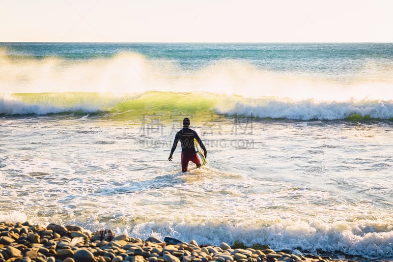 Surfer with surfboard go to ocean at sunset or sunrise