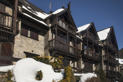 Horizontal shot of a row of semi-attached mountain apartments for skiers, covered by snow, on a sunny day, Gessa, Vall d’Aran, Lleida, Catalonia
