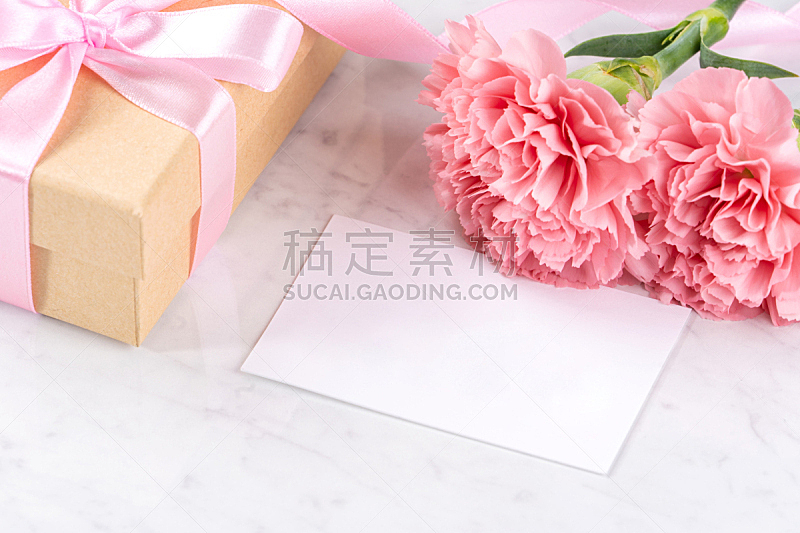 May mothers day handmade giftbox idea concept, beautiful blooming carnations with baby pink ribbon bow gift isolated on modern marble desk, close up, copy space, mock up