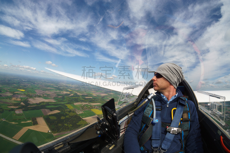 Blick auf den Piloten im Cockpit eines Segelflugzeuges im Fluge über Feldern als Luftaufnahme