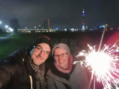 Young couple at night time holding a shiny sparkler in front of Düsseldorf skyline and rhine river