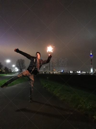 Young man posing with bright sparkler in front of Düsseldorf' skyline at night