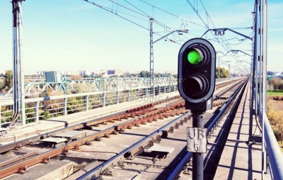 Traffic light in green on the subway tracks with catenaries on the tracks and blue sky in background